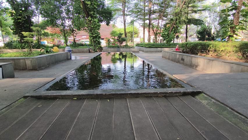 small pond in the middle of the garden with green trees in summer