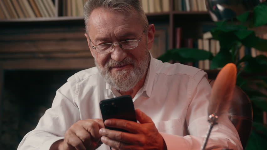Old Caucasian man using mobile phone smartphone male mature senior gadget businessman smiling digital device business home online internet social media chatting indoor office addict pensioner browsing