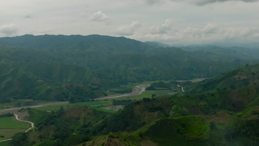 Mountain province with green hills and forest. Farm fields over the agricultural land near the river. Mindanao, Philippines.