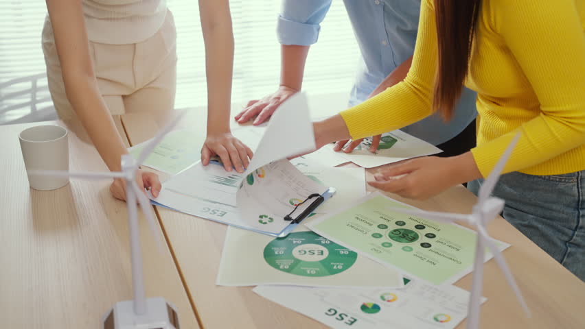 A group of business professionals stands in a modern corporate office, actively engaged in an ESG-focused brainstorming session, analyzing convergent strategies with agile planning methods while revie