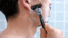 Man shaving with razor and shaving foam against blue tiles background in bathroom side view close-up. - Powered by Shutterstock - Get 15% off with code: PIKWIZARD15