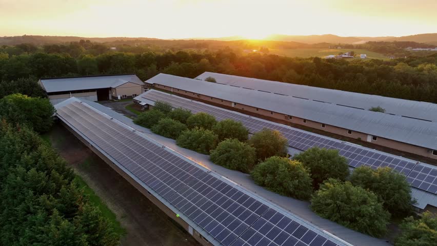 Long barn buildings in American countryside at sunset. Aerial backwards shot. Modern solar panels covering roofs. Green energy theme in rural area of USA.