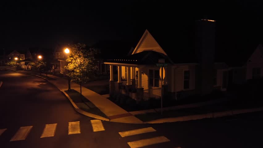 Traditional american front house porch at night. Aerial close up. Night scene with lighting lantern lights in neighborhood. Blooming trees outdoors on street.