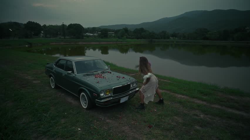 A touching emotional scene unfolds by an old car situated near the waters edge