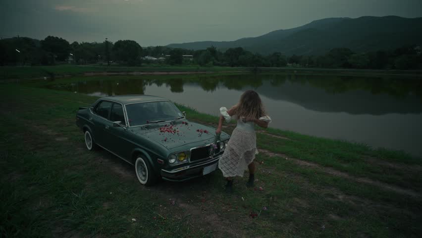 A touching emotional scene unfolds by an old car situated near the waters edge