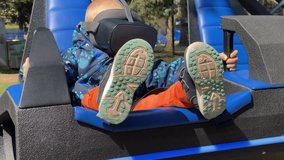 A child, wearing a virtual reality headset and a blue patterned jacket, is seated comfortably with their feet propped up on the blue footrest of a VR simulation ride - Powered by Shutterstock - Get 15% off with code: PIKWIZARD15