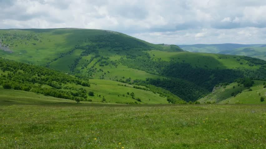 Green valley with rolling hills revealing gradual landscape transformation, dynamic shadows traversing verdant terrain under shifting cloudscape during daytime