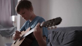 Teenage boy playing guitar while sitting on sofa at home, play the musical instrument. The concept of learning to play a musical instrument - Powered by Shutterstock - Get 15% off with code: PIKWIZARD15