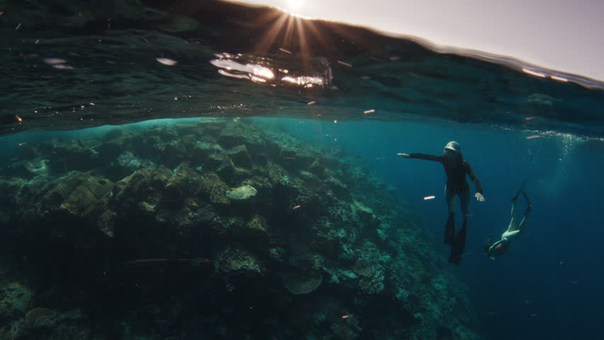 Splitted underwater shot of the shallow coral reef and freedivers swims underwater nearby. Komodo National Park, Indonesia