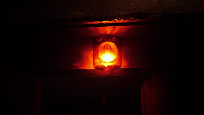 Close-up of a rotating red emergency siren lamp on the wall of a dark tunnel. A bomb shelter, an emergency signal on the wall during an air raid.