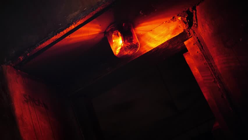 Close-up of a rotating red emergency siren lamp on the wall of a dark tunnel. A bomb shelter, an emergency signal on the wall during an air raid.