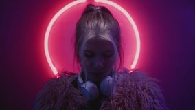Young woman DJ looking at the camera in the neon light of the night club. Portrait of a beautiful artist girl close-up. Lady in multicolor glow. Face of a female, put on white headphones. - Powered by Shutterstock - Get 15% off with code: PIKWIZARD15