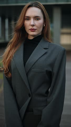 A fashionable Caucasian businesswoman holding a phone and tablet looks at the camera on a Seoul rooftop, her strong, pretty face revealed in a slow tilt-up and push-in shot