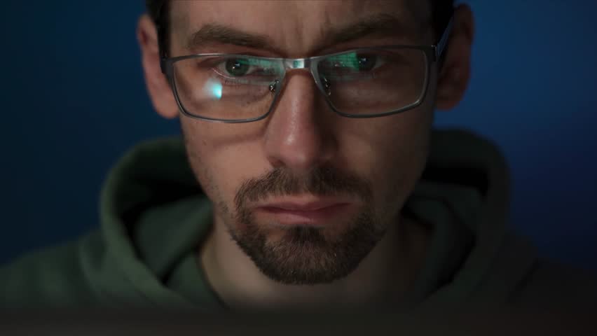 Close-up of a serious programmer, glasses reflecting programming code. Coder deeply focused on software engineering, analyzing data on his laptop screen