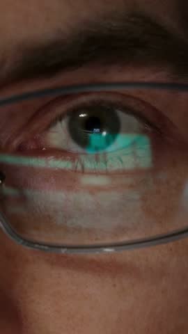 Extreme close-up of a programmer's eye with lines of code reflecting in eyeglasses, symbolizing AI development, cybersecurity, and machine learning in a digital world. Vertical video