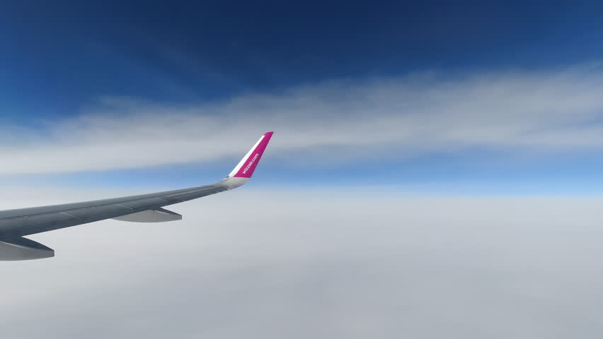 Stunning view of an airplane wing with pink winglet soaring high above white cloud layer against clear blue sky, captured during daytime flight through the atmosphere