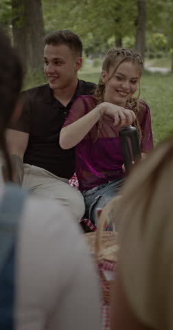 Friends enjoying a picnic in the park. They are laughing, talking, and eating snacks.