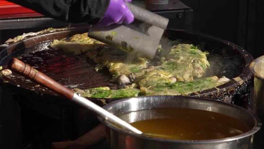 Slow motion of a vendor lifting steaming oyster omelet with spatula from pan at night market in Taichung, Taiwan