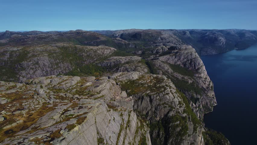 Sunlit aerial view of Preikestolen with fjord and peaks in the background, capturing Norway’s beauty.