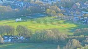 Aerial static shot of a cricket match in progress on a bright green pitch near Manvers Lake, Rotherham, with long shadows cast across the field and surrounding suburban buildings under the spring sun - Powered by Shutterstock - Get 15% off with code: PIKWIZARD15