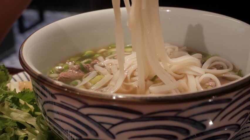 Freshly prepared Pho Bo noodles served in a bowl with beef, herbs, and garnishes