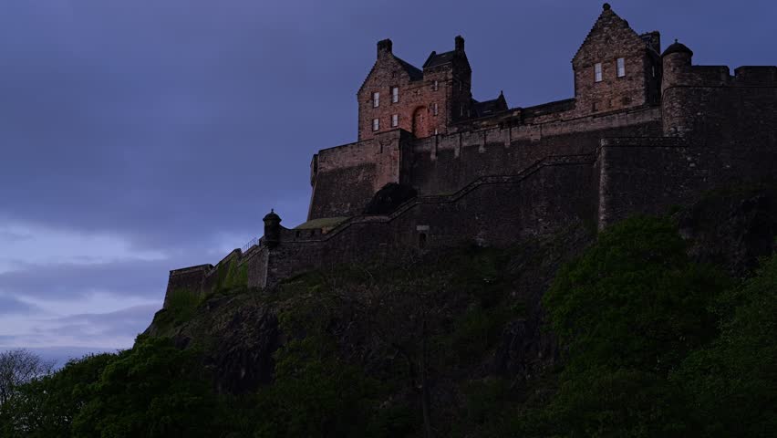 Beautiful Edinburgh castle silhouette at dusk with dark clouds in the sky. Historic landmark on top of the hill with few lights turned on. A popular tourist attraction. Edinburgh, UK, 05.04.2025