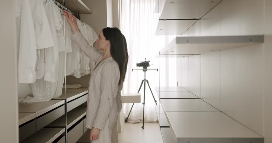 A woman stands in a modern walk-in closet filled with neatly arranged white clothes. The room is well-lit with natural light. Concept of organization, minimalism, and lifestyle.