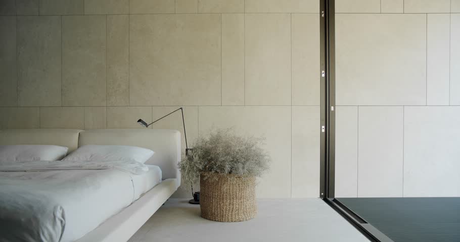 Explore this elegant minimalist bedroom featuring a white bed, large cushioned headboard, and natural light emanating from large sliding glass doors.