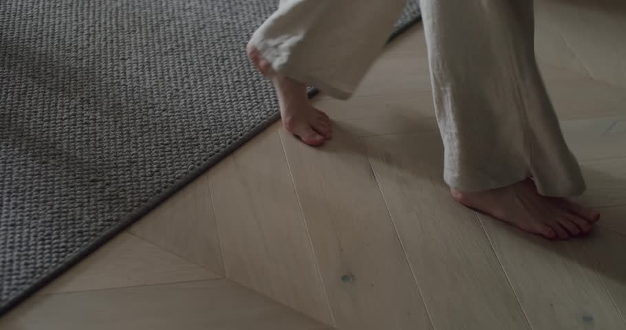 A close-up image showing bare feet stepping from a wooden floor onto a soft carpet, representing a cozy and comfortable home environment. Cozy Home Interior With Wooden Floor And Woven Rug