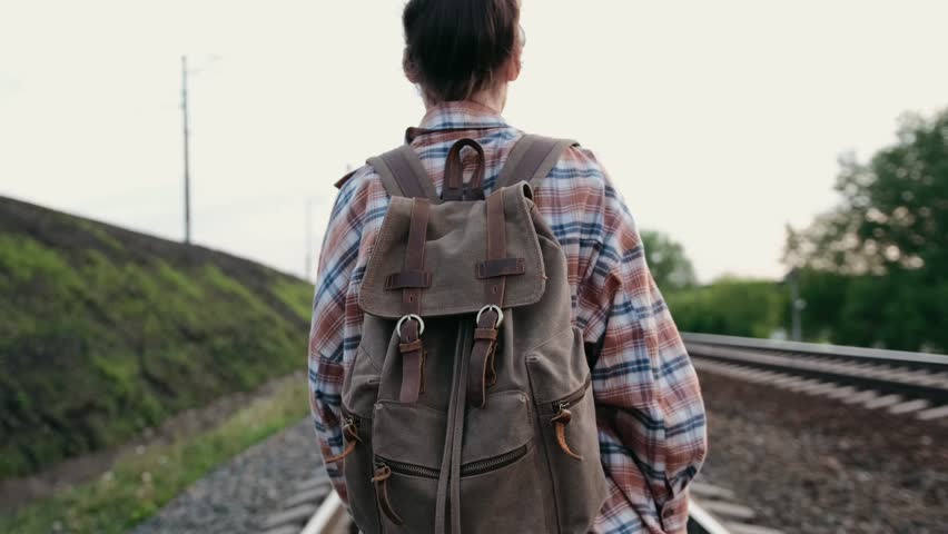A Woman Walking on Railway Tracks with a Backpack in a Beautiful Natural Setting