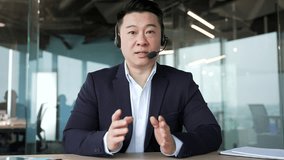 Webcam view. Confident asian businessman in headset talking on video call looking at camera sitting in office. Entrepreneur has a business meeting. The manager speaks remotely at an online conference - Powered by Shutterstock - Get 15% off with code: PIKWIZARD15
