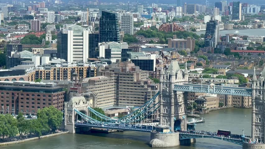 An iconic view of Tower Bridge spanning the River Thames, with the modern skyline of London in the distance, captured in full daylight from above, classic London at its finest, slow motion