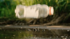 Plastic bottle falling into puddle creating splash drops ground view reflection slow motion summer sunset blurred background - Powered by Shutterstock - Get 15% off with code: PIKWIZARD15