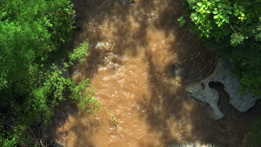 Aerial drone view captures a rushing river flowing over rocks surrounded by vibrant green foliage, highlighting the dynamic interaction between water and forest in a natural landscape. Thailand.
