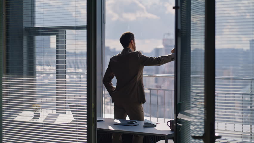 Corporate leader watching skyline reflecting ambitions during day moment. Thoughtful executive wearing formal clothes gazing outside glass facade. Worried sad worker considering decision in workplace