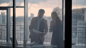 Two confident partners discussing contract papers standing at office window. Serious smart colleagues doing paperwork at grey cityscape. Couple businesspeople coworkers work together at private room - Powered by Shutterstock - Get 15% off with code: PIKWIZARD15