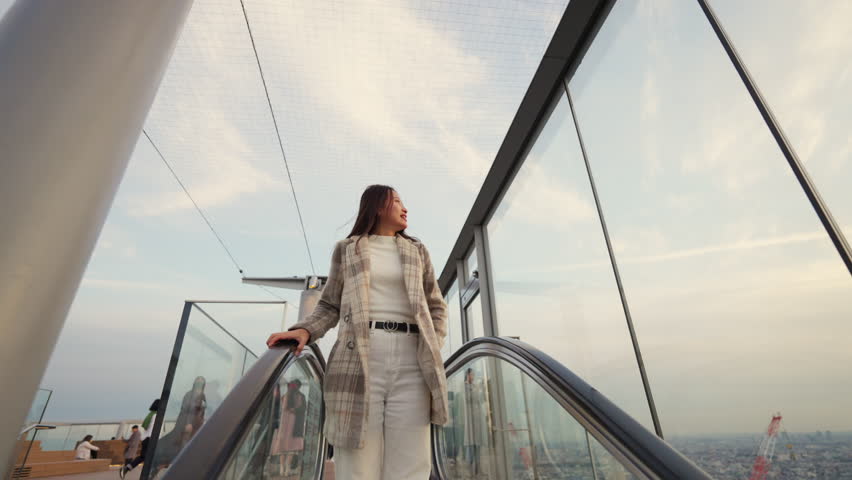 Happy Asian woman looking cityscape while travel at skyscraper building rooftop in Shibuya, Tokyo city, Japan at sunset. Attractive girl enjoy outdoor lifestyle on autumn winter holiday vacation.