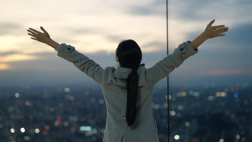 Happy Asian woman looking beautiful metropolis cityscape at skyscraper building rooftop at sunset. Attractive girl relax and enjoy outdoor lifestyle travel and shopping in the city on holiday vacation