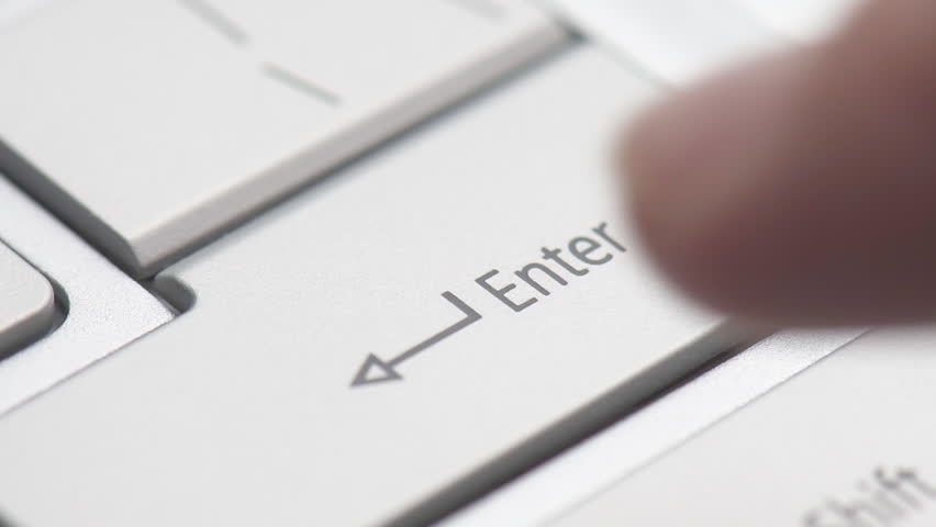 Macro shot of finger pressing Enter button on a laptop keyboard.