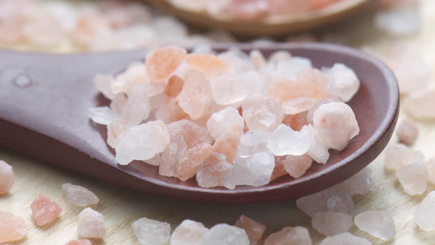 Closeup view of wooden spoons with Himalayan salt crystals. Natural rock salt (halite) of pinkish tint from Punjab region of Pakistan. Macro shot.