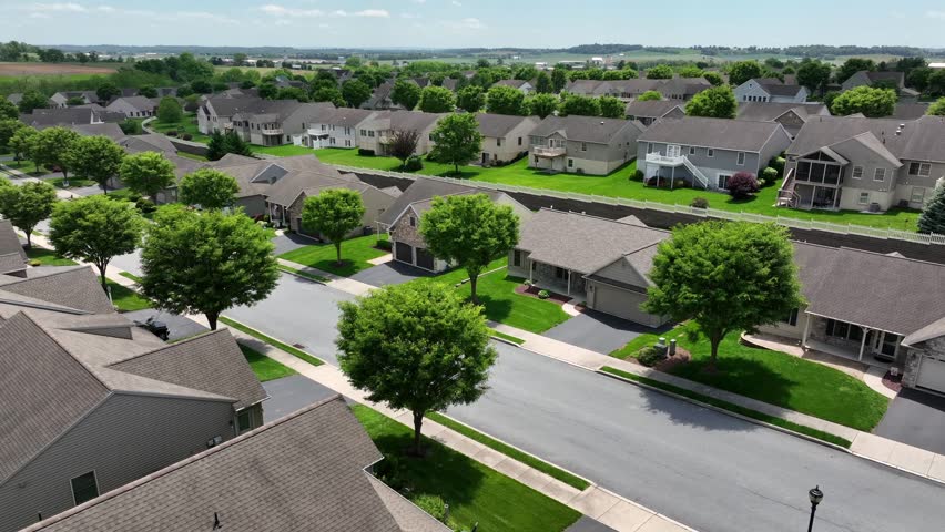Tree-lined street of upper class housing area in America. Sunny day with green trees in rural area of USA. Aerial approaching wide shot. Single Family houses with garages in quiet suburbia.