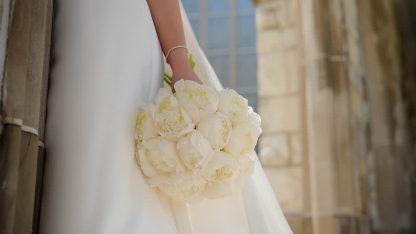 Bride holding white wedding bouquet and wind is waving her dress .