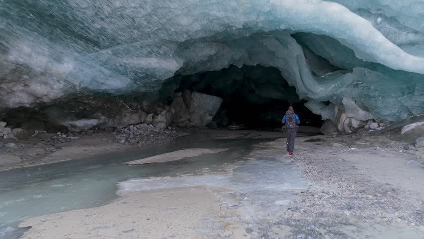 Person explores Morteratsch glacier ice cave, walking along meltwater stream, Stunning ice formations, ideal for adventure, nature documentaries, Switzerland