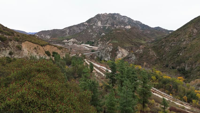 Aerial view of Big Tujunga Bridge and Josephine Peak in Angeles National Forest, California, showcasing vibrant fall foliage and majestic mountain landscapes.