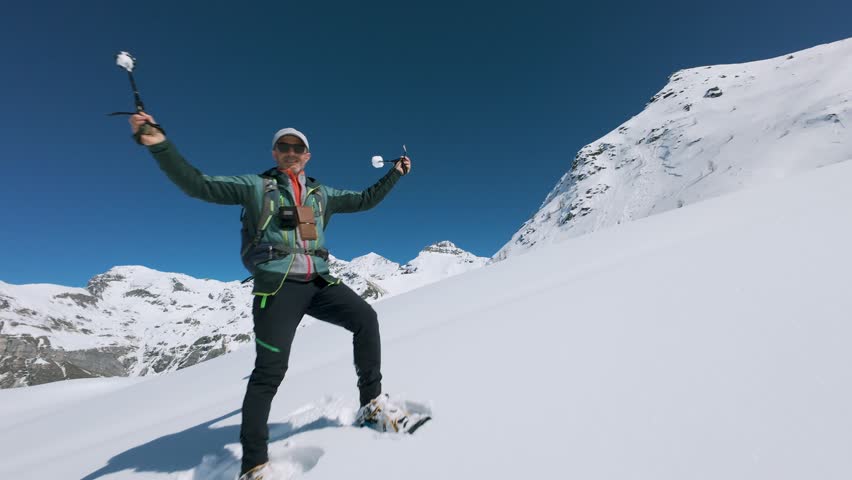 FPV drone follows adventurer snowshoeing uphill on pristine snowy mountain in Cheneil, sunny day, blue sky, footprints in deep snow, Ideal for winter sports, adventure. Italy. Aerial, copy space