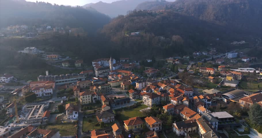 Charming Pella town on shores of Lake Orta, mountains in background, hazy morning or afternoon light, Italian lakes, Italy. Aerial backward