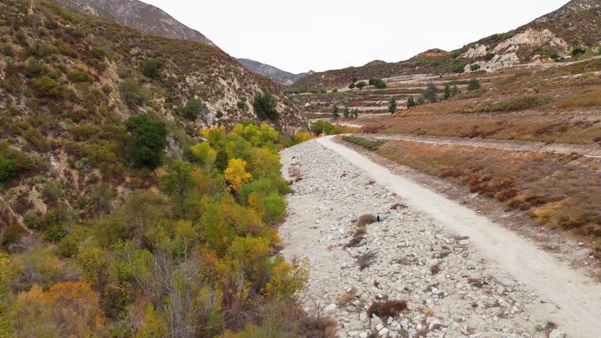 Aerial view flying under Big Tujunga Bridge in Angeles National Forest, California, showcasing vibrant fall foliage and majestic mountain landscapes.
