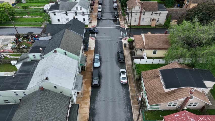 Drone flight over small american town with row of houses in different styles and colors. Car crossing road. Aerial top down flyover. Cloudy spring day in Pennsylvania USA.
