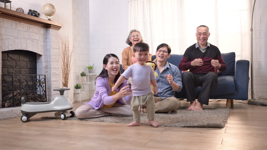 Happy multi-generational Asian family enjoying quality time together at home, cheering and smiling with a toddler