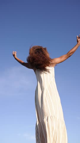 Confident young woman dances with freedom and joy against a clear blue sky, embodying a carefree and lively spirit